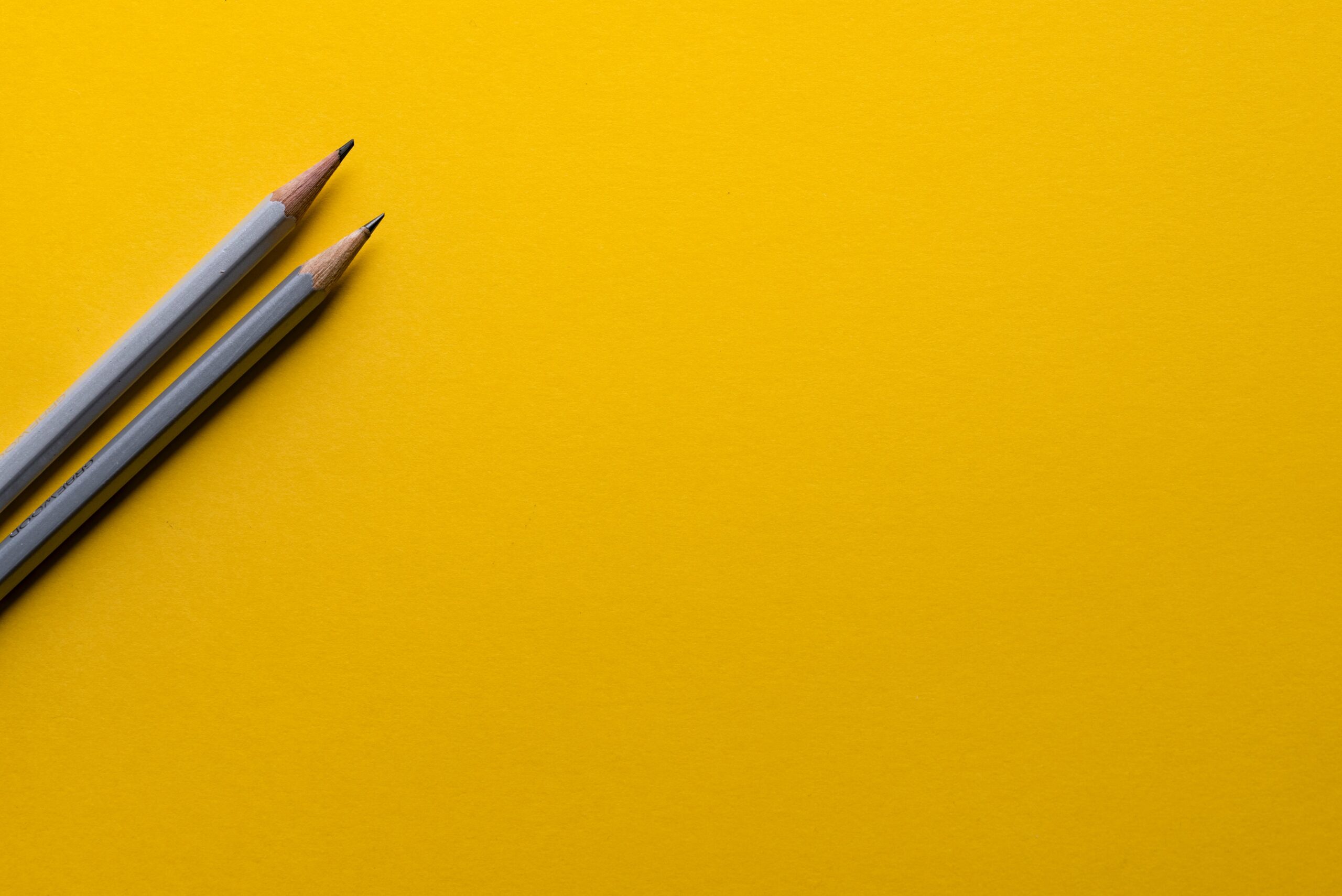 Two sharp pencils laying on a yellow background