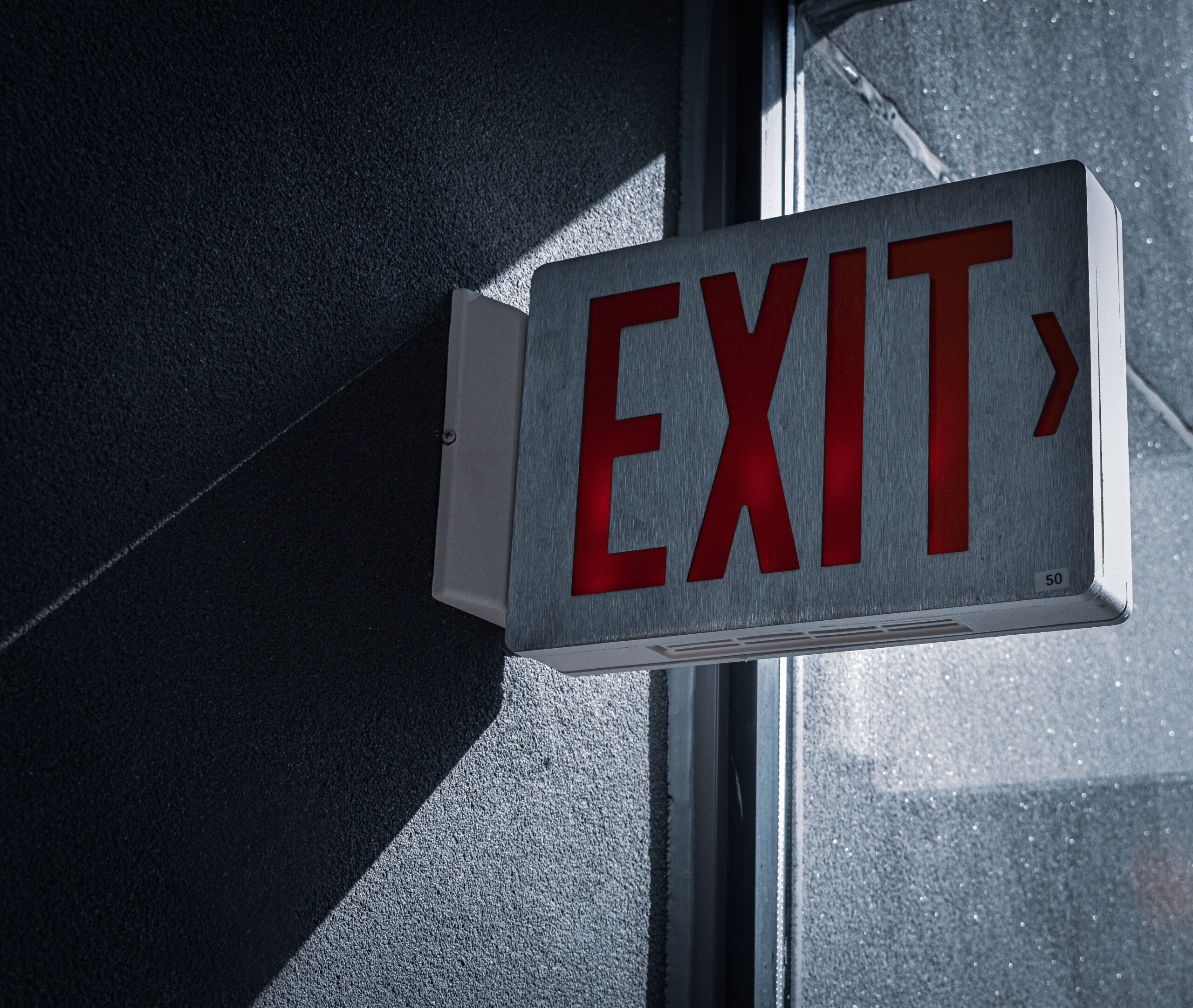 Grey sign on grey wall with word "exit" written in red