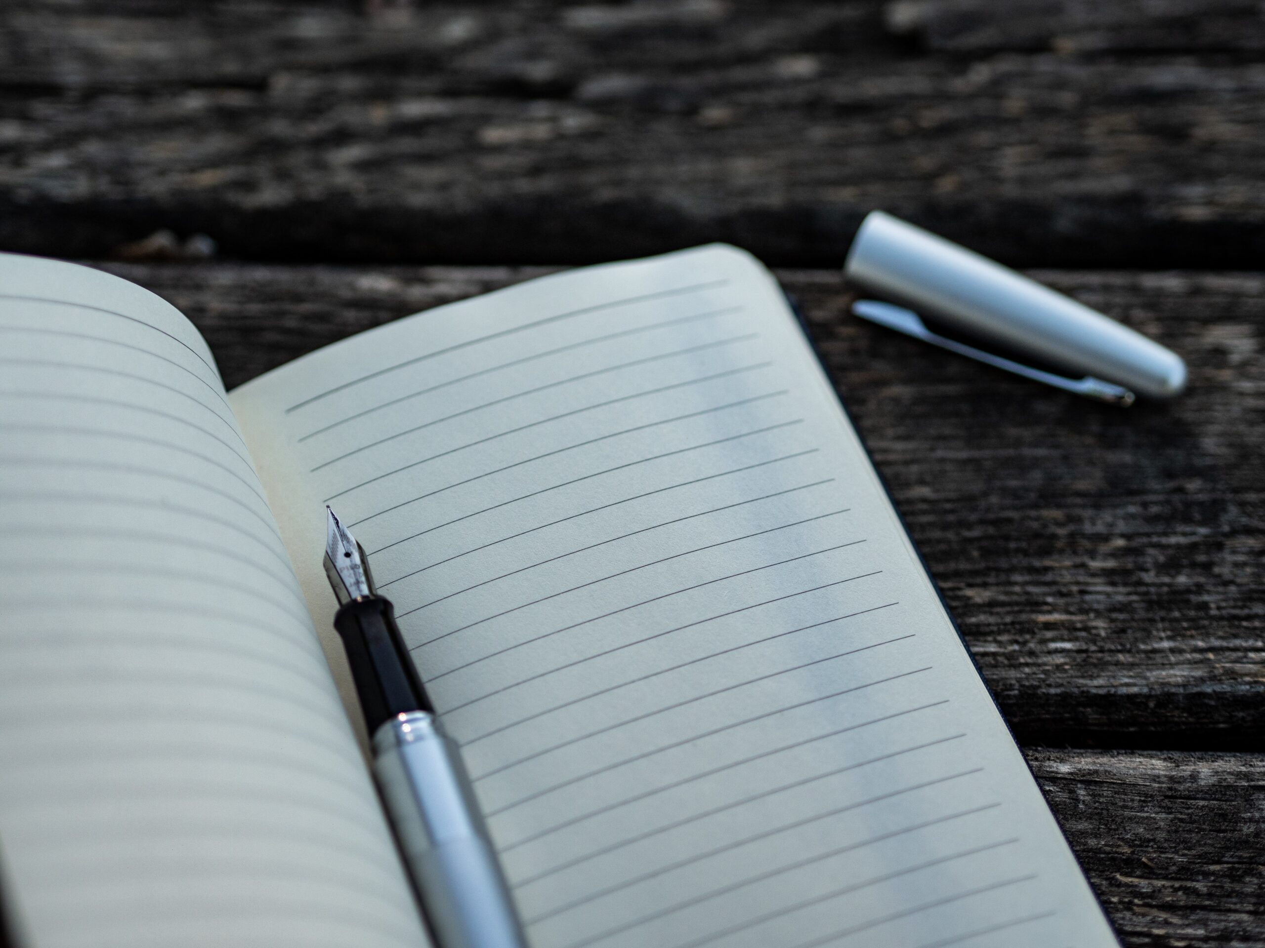 A fountain pen with lid off lying in an empty open notebook