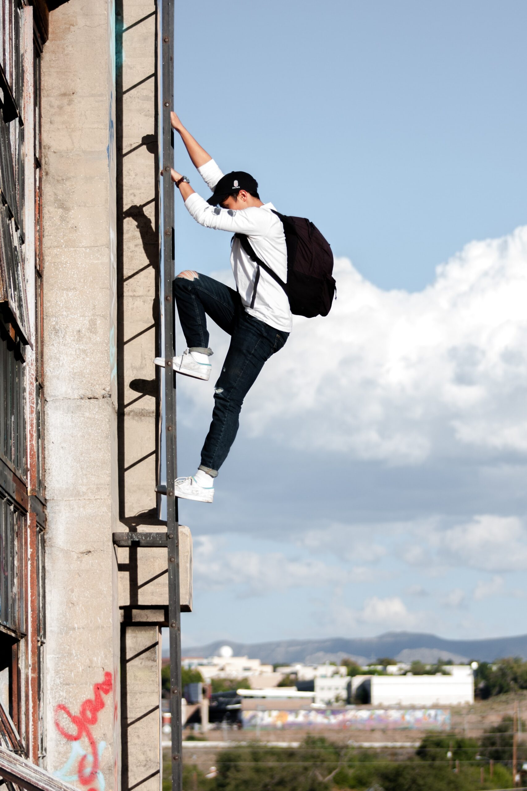 Man with a backpack climbing up a ladder on the outside of a building