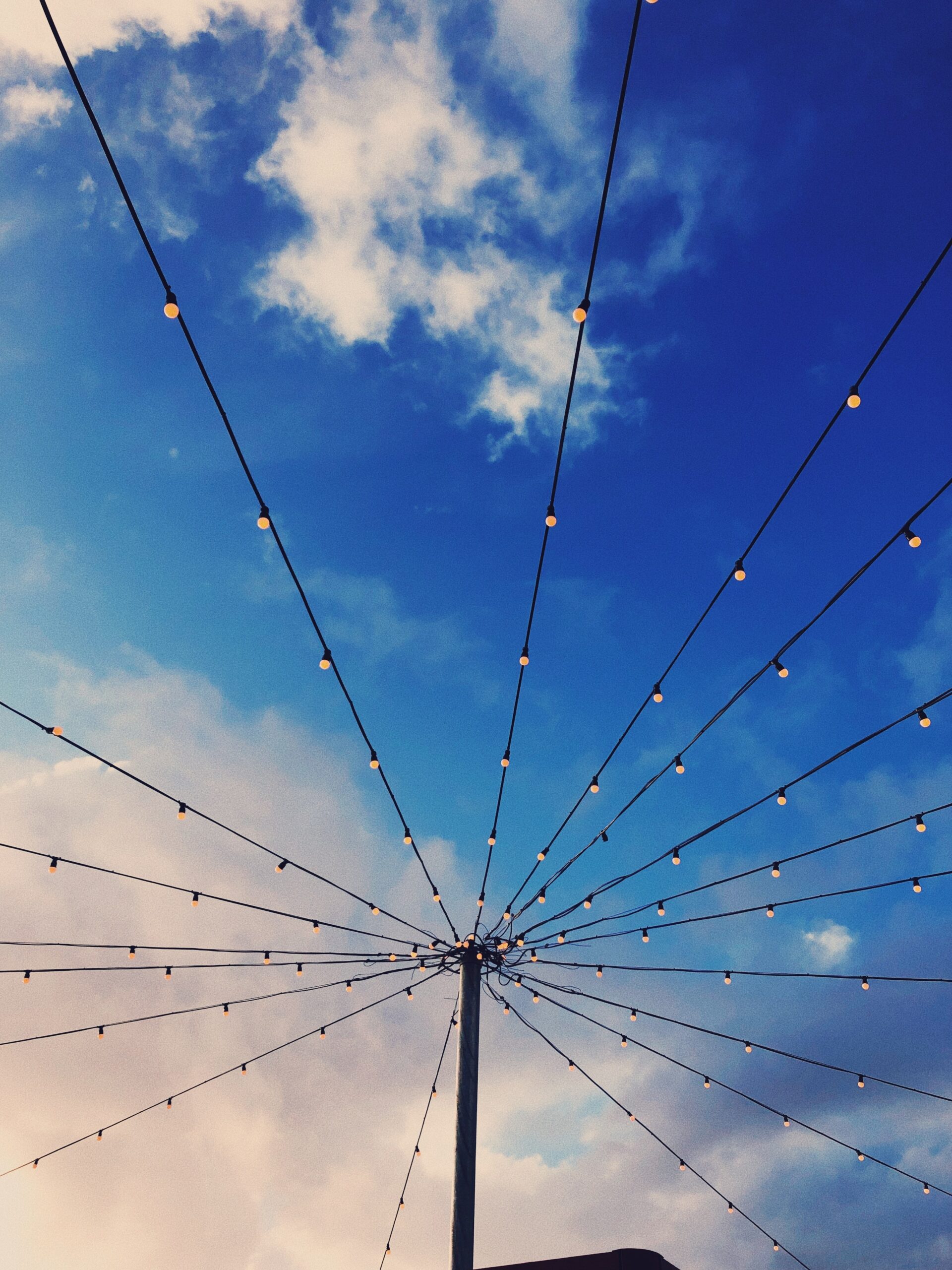 A post with strings of lights coming out from all sides, set against a bright blue cloudy sky