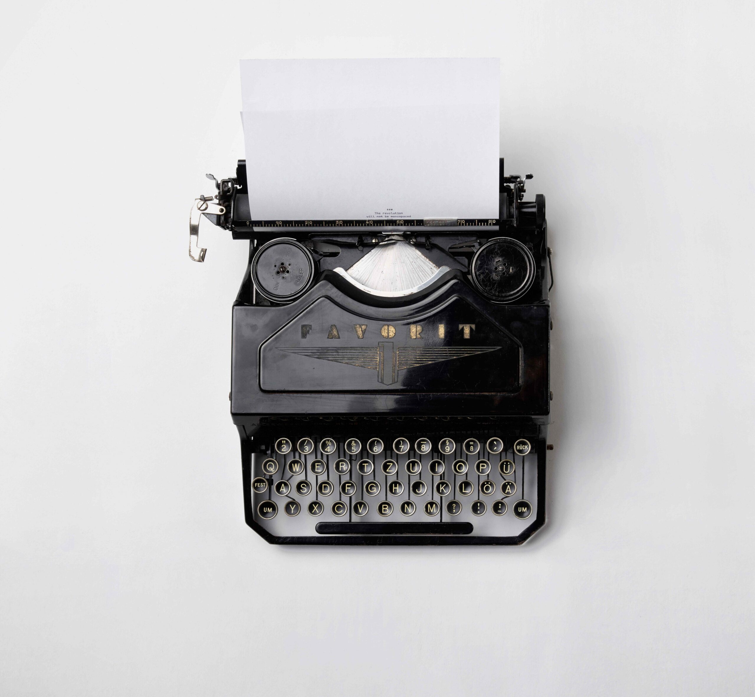 A black typewriter with a piece of blank white paper ready for typing, against a white background