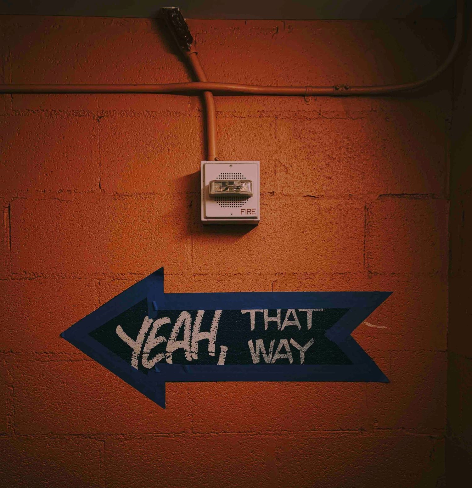 A dark orange wall with a hand painted arrow that reads "yeah, that way"