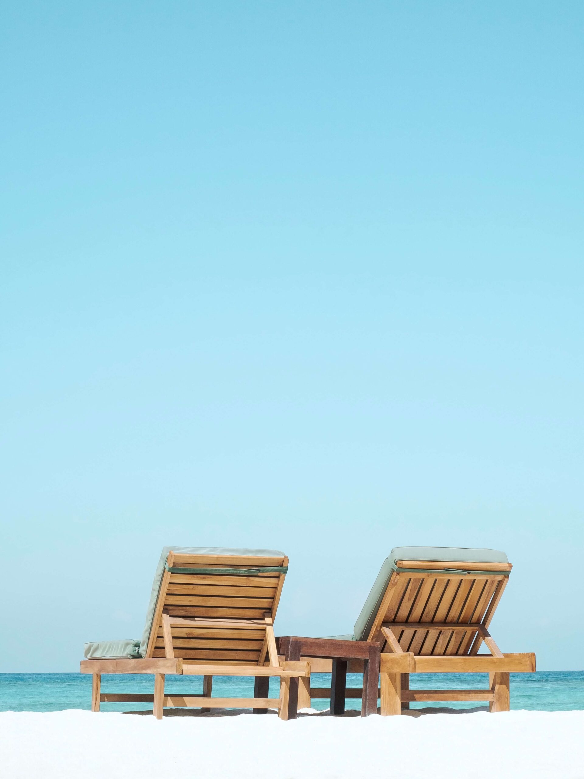 Two wooden chairs on a beach facing a clear sea