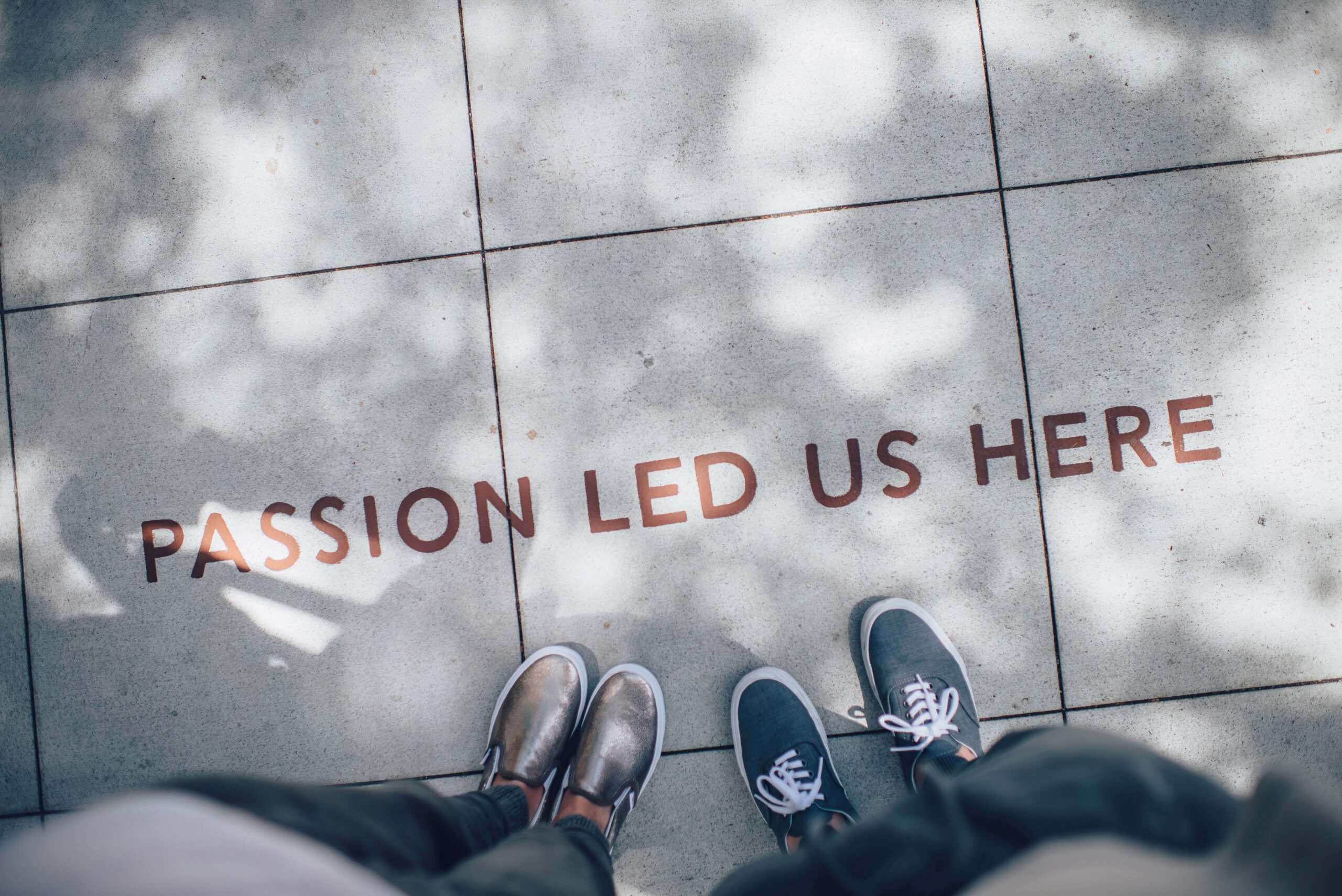 Looking down at two sets of legs and shoes on a tiled floor with gold letters across the floor reading "passion led us here"