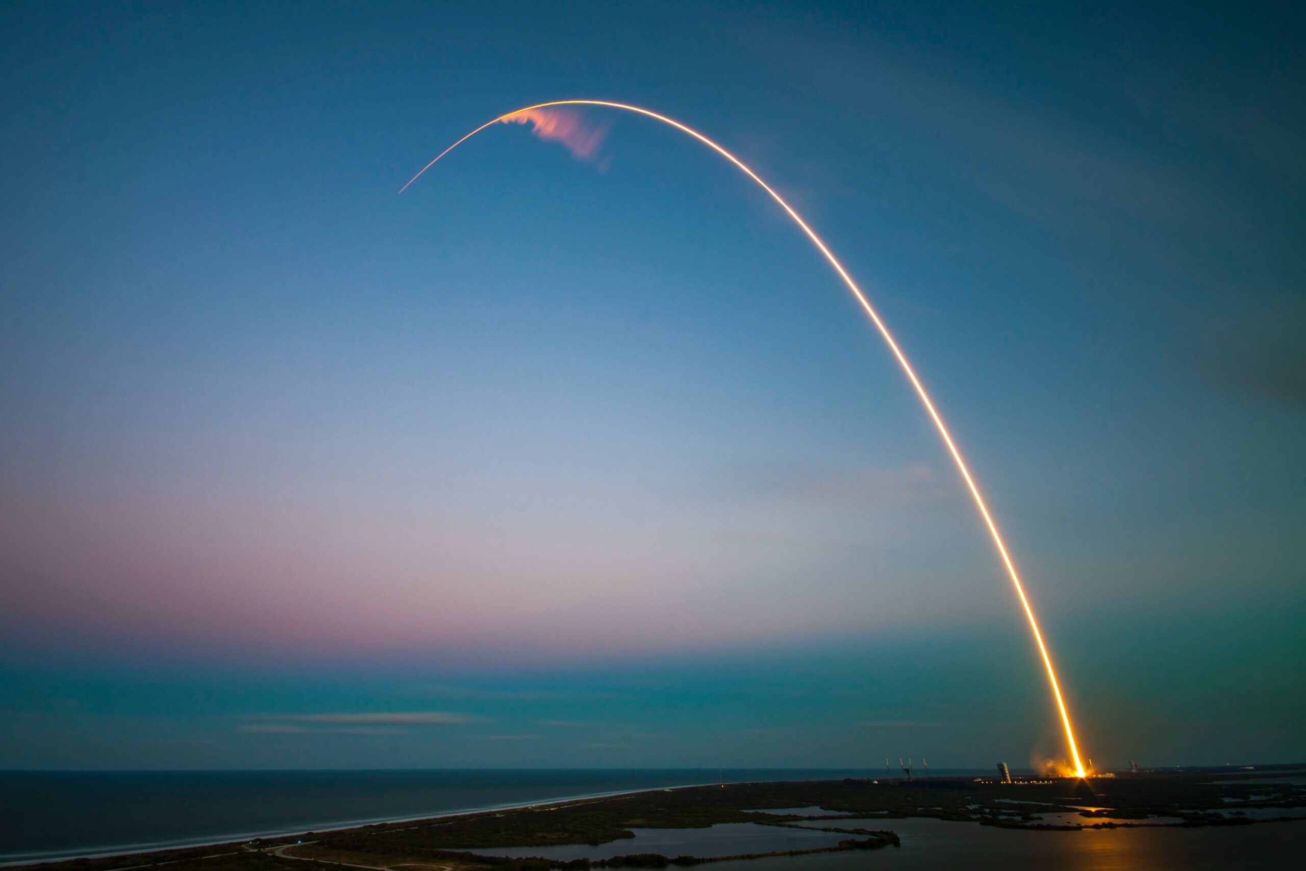 A rocket in the distance launching in a orange arch against a dark blue sky