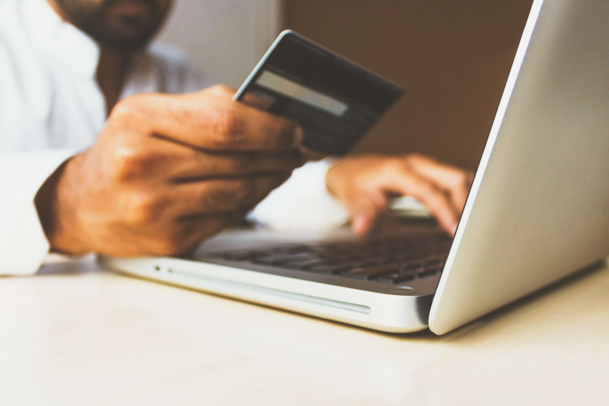 Someone holding a bank card in front of a laptop and typing card details in