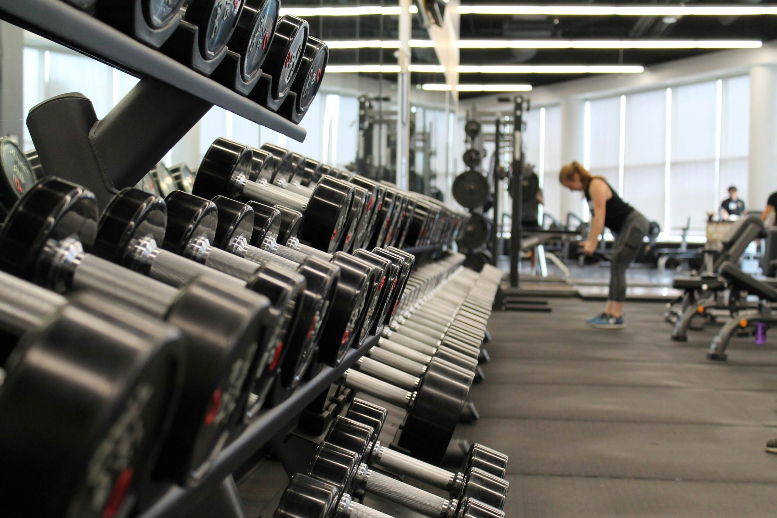 Woman lifting weights against a large rack of hand weights in a gym