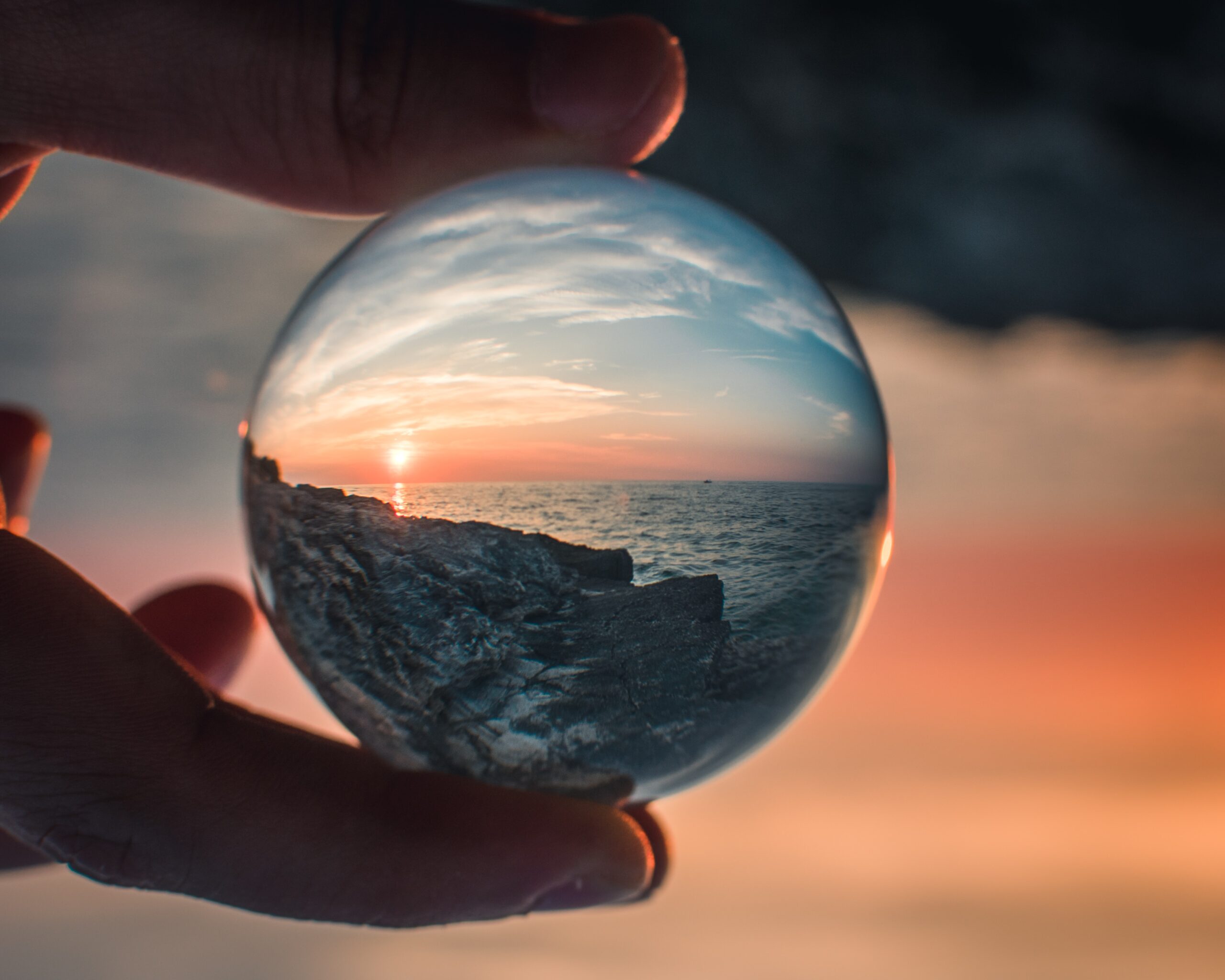 Someone holding a glass ball in front of a sunset so the image is reflect in the ball